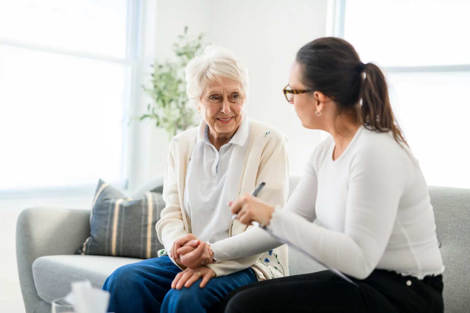 senior woman holding the hand of adult woman on couch